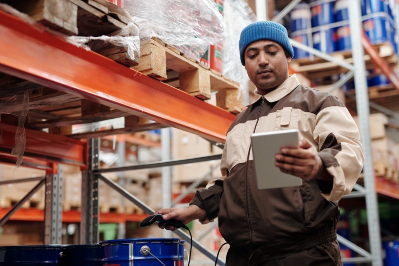 A man holding a tablet connected to a handheld scanner, logging items in a warehouse